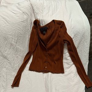 A simple burnt orange cardigan that has six buttons and ruffles at the end.
